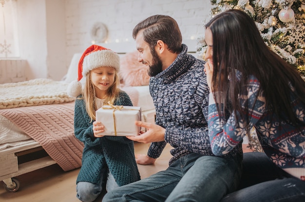 Merry Christmas and Happy Holidays Cheerful Mother, father and her cute daughter girl exchanging gifts.