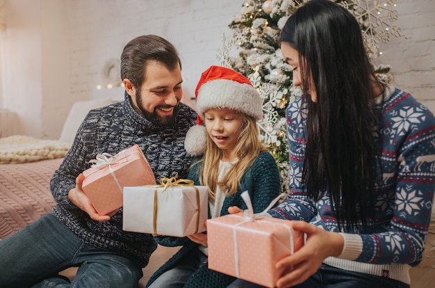 Merry Christmas and Happy Holidays Cheerful Mother, father and her cute daughter girl exchanging gifts.