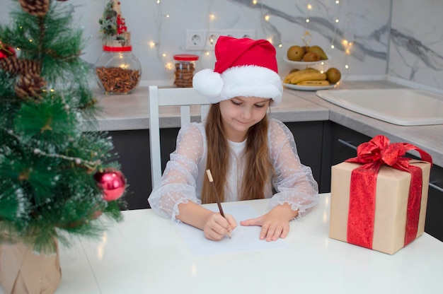 Merry Christmas and Happy Holidays. Cute little girl writes letter to Santa Claus at home at the table. Holiday, childhood, winter concept of celebration. Selective focus.