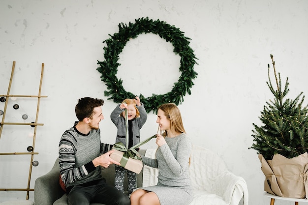 Merry Christmas and Happy Holidays Mom dad gives a gift to her daughter near the Christmas tree Cheerful mother father hugging cute baby child girl together at home Happy New Year 2021