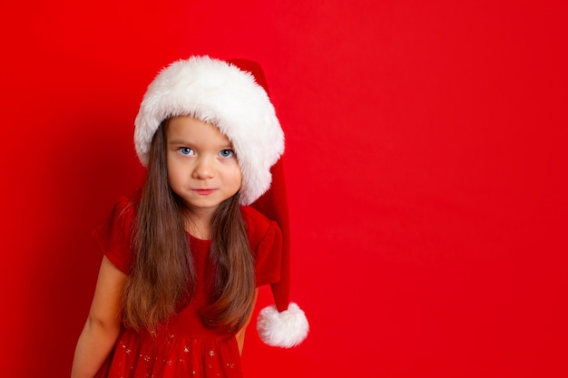 Merry Christmas and happy holidays Portrait of  emotional girl in a Santa cap on a red background