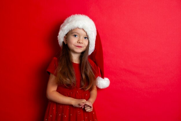 Merry Christmas and happy holidays Portrait of a girl in a Santa cap on a red background Children