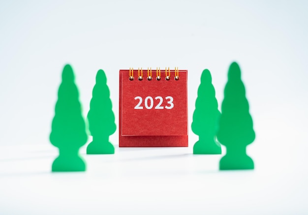 Merry Christmas and Happy new year 2023 background minimal style 2023 numbers year on small red desk calendar cover with christmas tree models isolated on white background