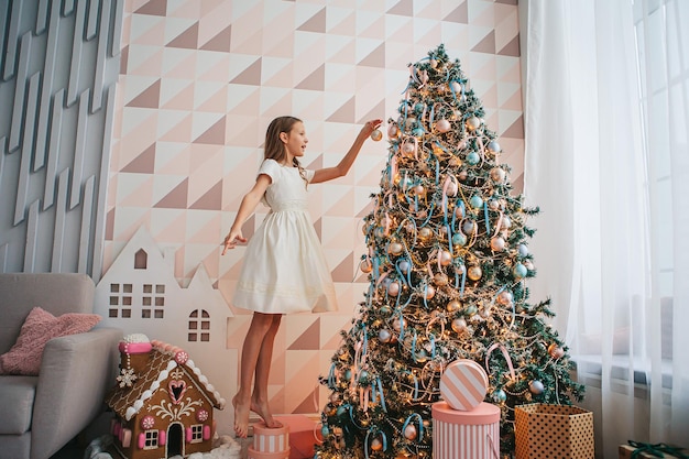 Merry Christmas and Happy New Year. Adorable little girl decorating the tree indoors. The morning before Christmas