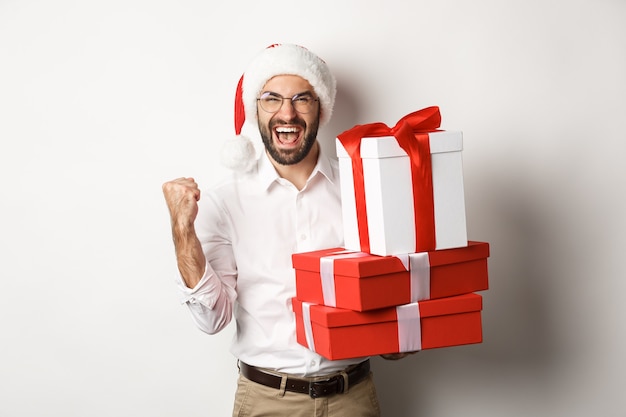 Merry christmas, holidays concept. Excited man receiving xmas gifts and rejoicing, wearing santa hat, celebrating New Year, white background