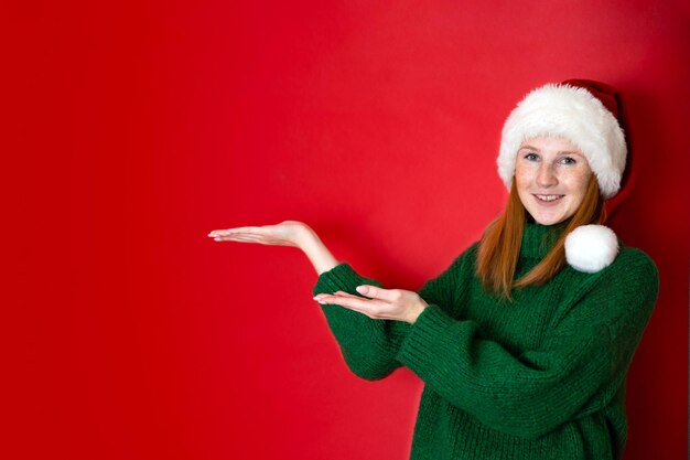 Merry Christmas Portrait of a beautiful young teenage girl in a cozy knitted green sweater and Santa39s hat The red background is the place for the text