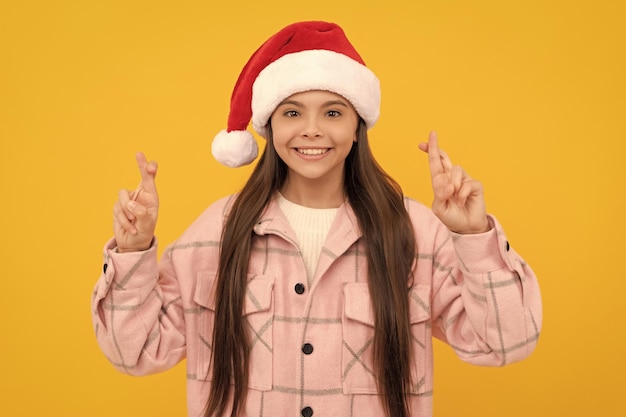 Merry christmas smiling kid in santa claus hat crossed fingers for luck teen girl