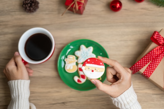 Merry Christmas with woman hand holding coffee cup and homemade cookie on table. Xmas eve, party, holiday and happy New Year concept