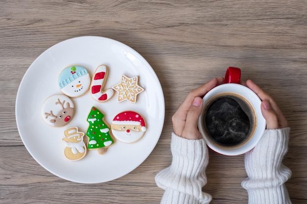 Merry Christmas with woman hand holding coffee cup and homemade cookie on table. Xmas eve, party, holiday and happy New Year concept