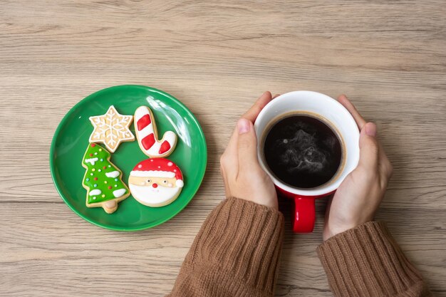 Merry Christmas with woman hand holding coffee cup and homemade cookie on table. Xmas eve, party, holiday and happy New Year concept