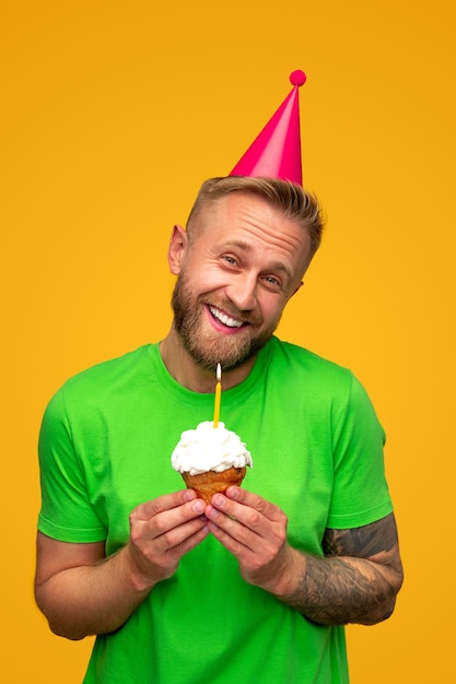 Merry guy in cap holding birthday cupcake