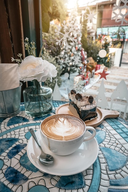 Merry xmasHot coffee latte with latte art milk foam in cup mug and Homemade chocolate cake with Xmas decors and Xmas tree baubles on marble floor desk Celebrating Merry Christmas and New year