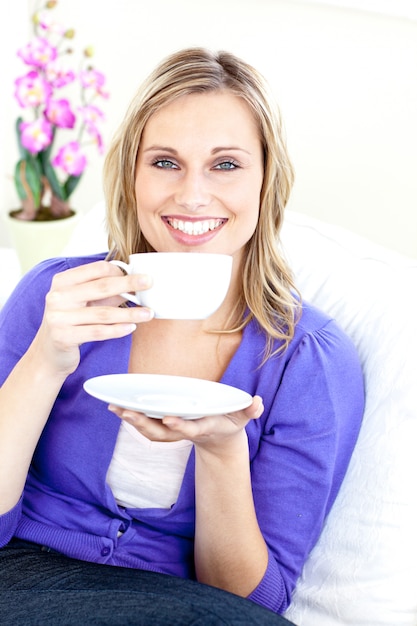 Merry young woman holding a cup of coffee on a sofa