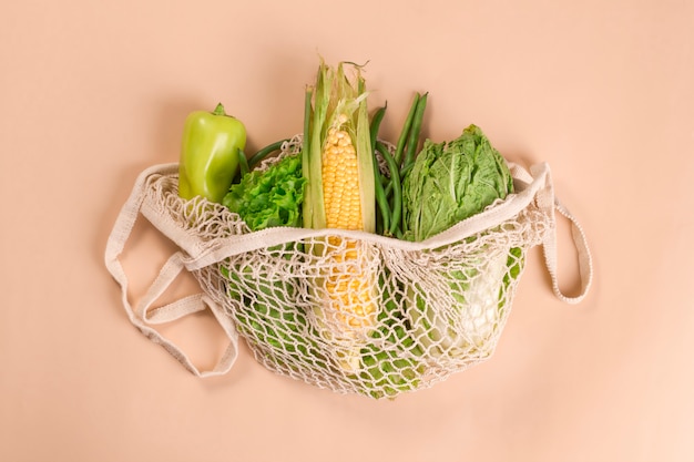 Mesh string bag with green vegetables on a beige background. 