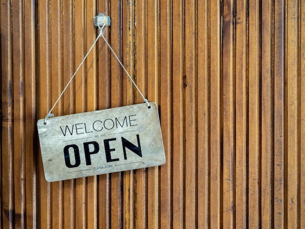 Message Welcome we are open please come in on old and dirty wooden sign hanging on wood wall background with copy space Sign board in front of the store cafe or coffee shop