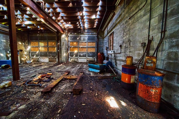 Messy abandoned interior of mechanic shop with garage doors and rusted barrels