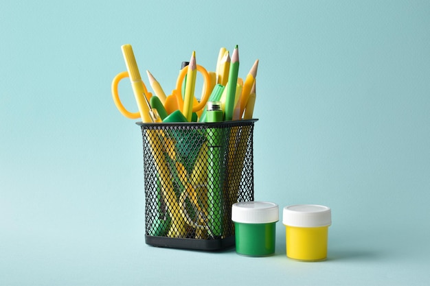 A metal black jar with yellow and green colors and pens and pencils on a light blue background School supplies space for copying