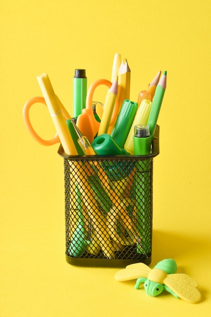 Metal black jar with yellow and green pens paints and pencils on a yellow background