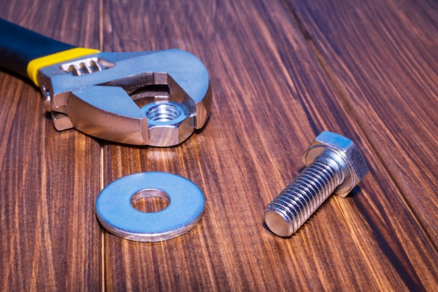 Metal bolt and nut on vintage wooden background with adjustable wrench