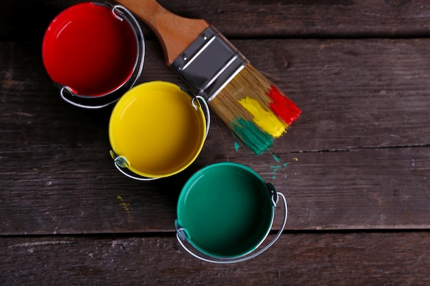 Photo metal buckets with colorful paint near brush on wooden background