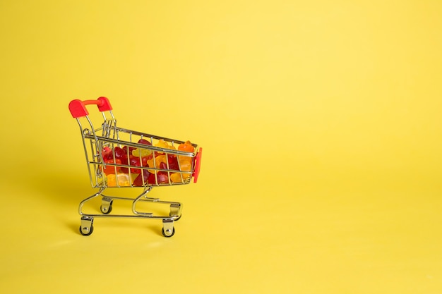 Metal cart with marmalade in the shape of bears on a yellow isolated background with space for text