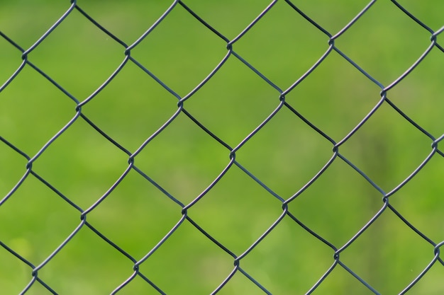 Metal chain-link fence on a green grass background 