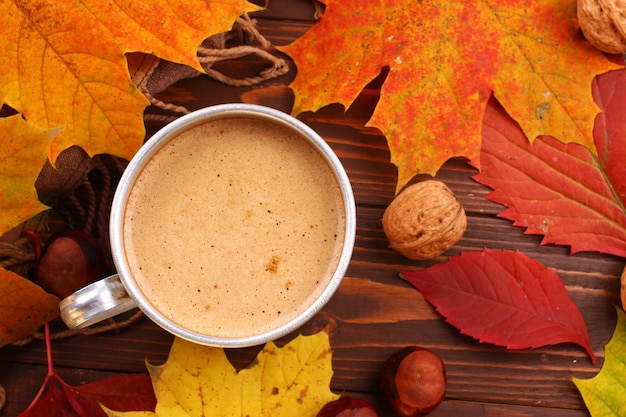 Metal cup with cappuccino, walnut and autumnal leaves