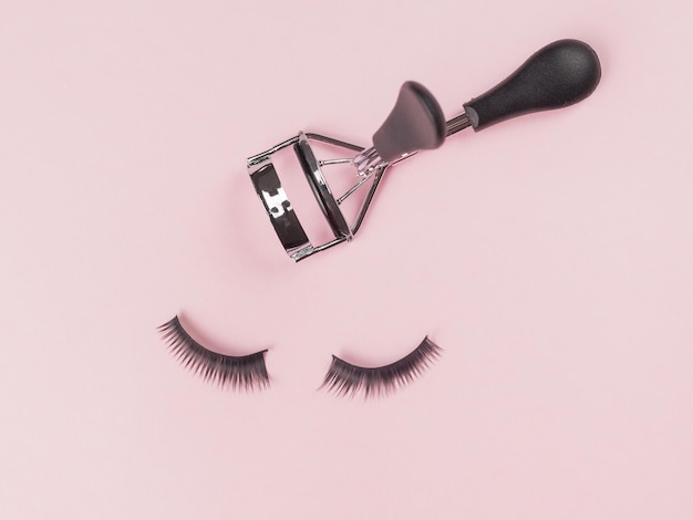 Metal eyelash curlers and a pair of false eyelashes on a pink background