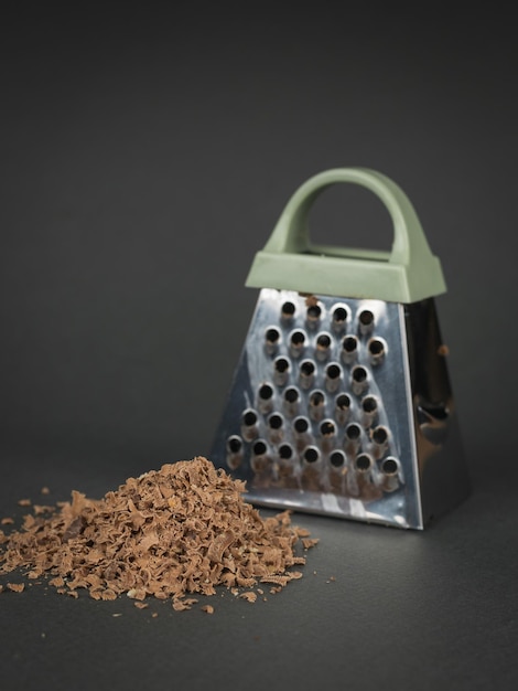 Metal grater and grated chocolate on a gray background