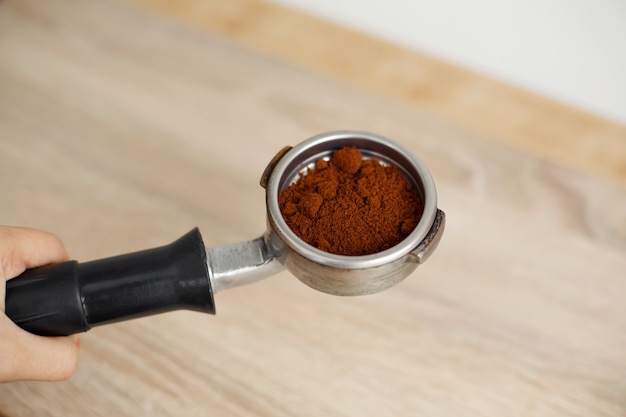 Metal holder for the coffee machine with ground coffee inside lies on a wooden table