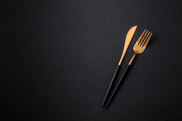 Metal kitchen knife and fork on a dark textured concrete background