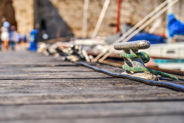 Photo metal mooring bitt with rope on wooden pier at blue sea water under bright sunlight close view