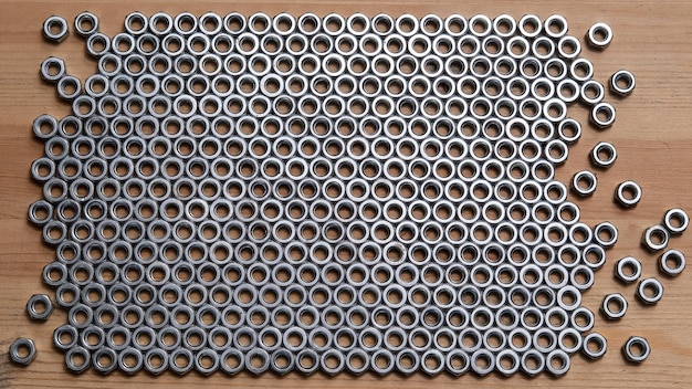 Metal nut are neatly stacked on a wooden table in the form of a frame