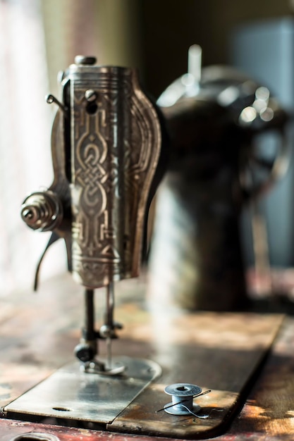 Metal reel of thread and a needle is on the table antique sewing machine in the sun.