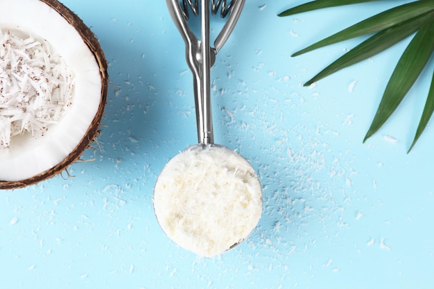 Metal scoop with fresh ice cream and desiccated coconut in half of nut on color background