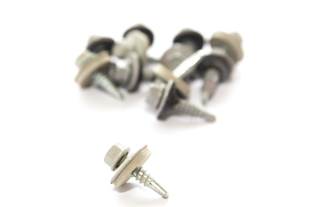 metal screw in close-up with pile of screws out of focus background on white background