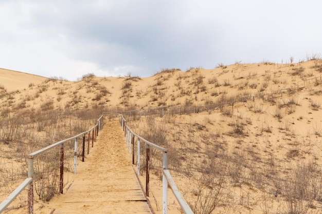 A metal staircase rises to a sand dune Climbing to the top there is a lot of sand in the desert