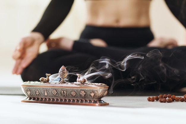 Metal stand for incense with smoke on the surface of a meditating person in the lotus position