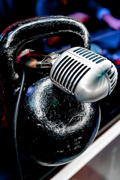 Metal vintage microphone lies on a black sports kettlebell in the institution. High quality photo