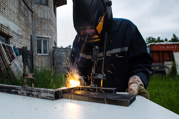 Metal welder working with arc welding machine to weld steel at factory while wearing safety equipment.