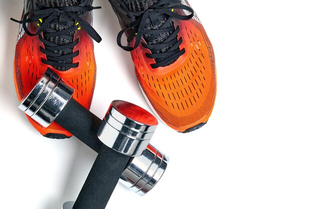 Metallic heavy dumbbell dropped on leg in orange sneaker isolated on white background