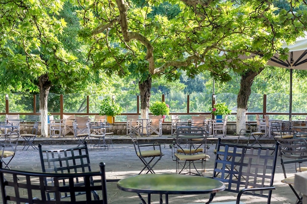 The metallic tables and chairs of a street caferestaurant under the big sycamore trees on a sunny summer day Tzoumerka Epirus Greece