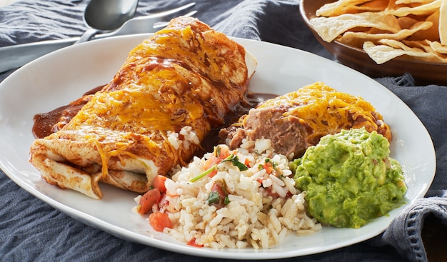 Mexican burrito platter with red enchilada sauce, fried beans, rice and guacamole