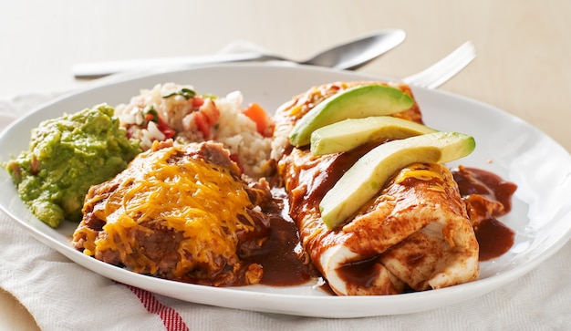 Mexican burrito platter with red enchilada sauce, fried beans, rice and guacamole