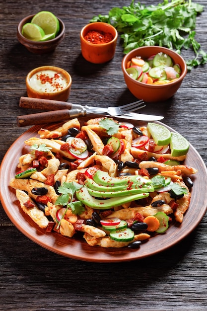 Mexican chicken salad of black beans cilantro radish carrot cucumber and avocado with tahini dressing and chili served on brown plate on rustic wooden background top view closeup