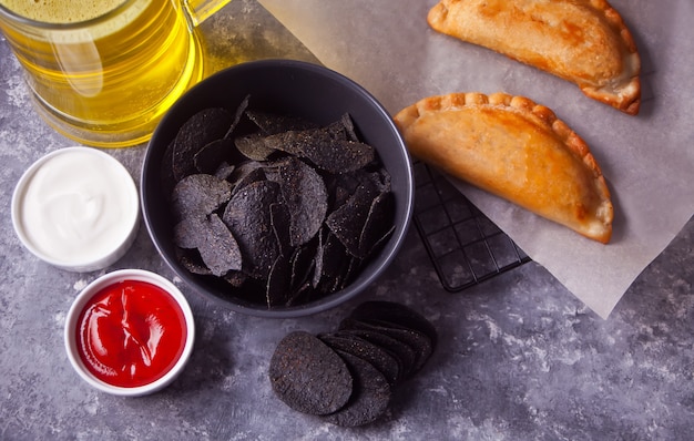 Mexican corn chips nachos and fried meat pies empanadas cheburek with dips. Black chips nachos for brutal men. Top view.