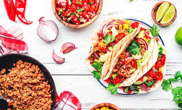 Mexican cuisine Tacos with beef corn red beans tomato salsa sauce and onions in corn tortilla on plate White table background top view