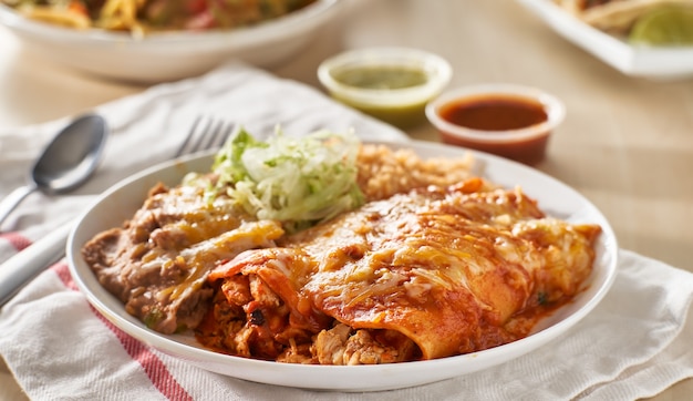 Mexican enchilada platter with red sauce, fried beans and rice