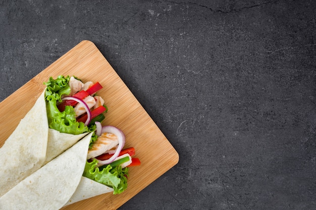 Mexican fajita with chicken, peppers, onion and lettuce on slate background