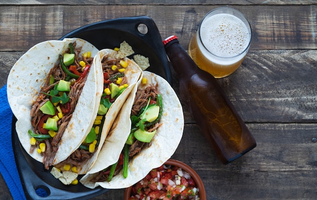 Mexican fajitas with beer on a black tray on wooden boards. Copy space. Mexican food concept.